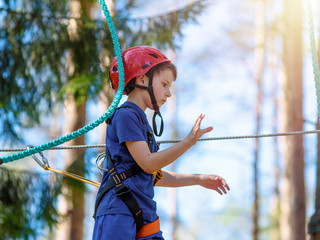 Boy in helmet is doing activity in adventure rope park with all climbing equipment.