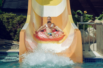 Boy with mom on floater sliding down slide in waterpark. - 277753237