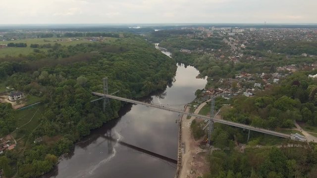 High pedestrian suspension cable bridge across the river in Zhytomir, Ukraine. Summer city urban river landscape. Aerial survey, flight of drone