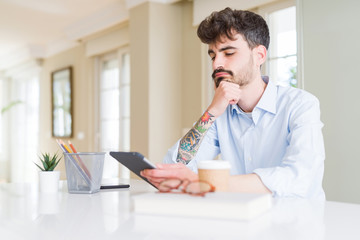 Young business man using touchpad tablet serious face thinking about question, very confused idea