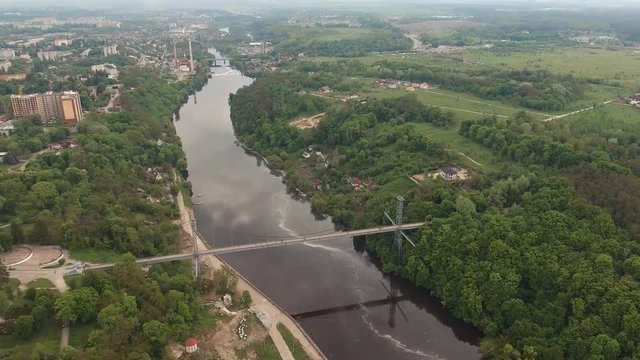High pedestrian suspension cable bridge across the river in Zhytomir, Ukraine. Summer city urban river landscape. Aerial survey, flight of drone