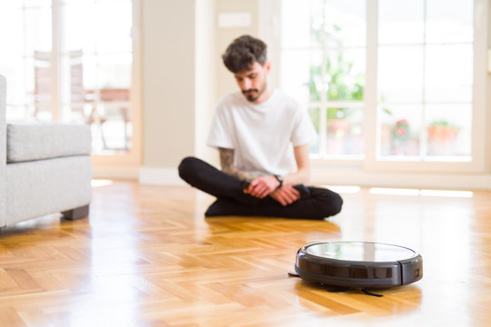 Young man using automatic vacuum cleaner to clean the floor, controling machine housework robot