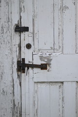 This tarnished old white door has black hardware.