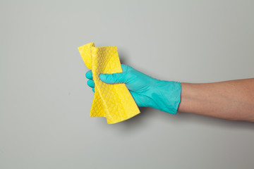 Hand in rubber glove holding cleaning sponge. Hand of chambermaid on gray background. Space for text.