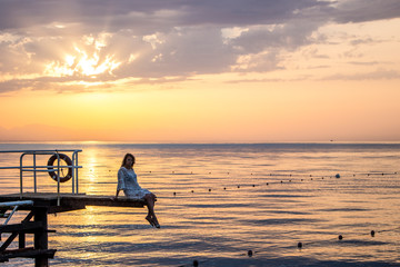 The girl sits on the edge of the pier admiring the dawn and the sea.