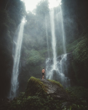 From below view of man standing on rock among high green cliffs with waterfall, Bali