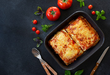Homemade Italian Lasagna with Tomato Sauce and Chicken, Served with Tomatoes and Basil. Two portions. Dark background. Top view. Copy space