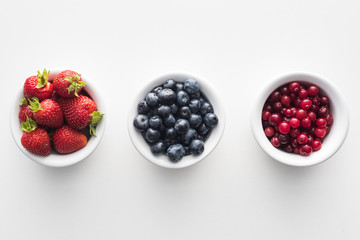 top view of sweet cranberries and blueberries, strawberries on white bowls
