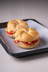 Two homemade burger Vienna Kaiser bread bun bread roll with chicken meat tomato mustard mayonnaise on baking tray sheet parchment paper white background