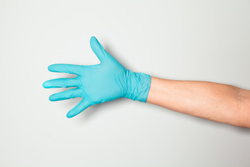 Hand in blue silicone glove on grey background shows the sign OK.