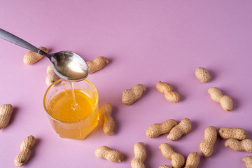 Honey liquid in glass with metal spoon with peanuts minimal on purple background backdrop food nut texture copy space
