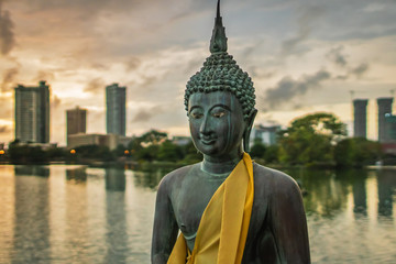 Statue of Buddha made of bronze in a peacefull pose, in front of a cityscape on the Beira Lake in...