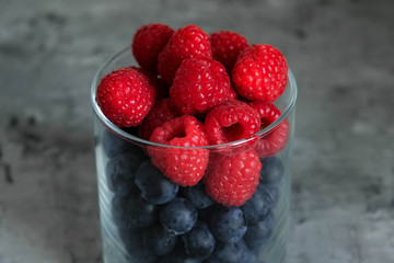 Fresh blueberries and raspberries in a wooden eco-friendly plate on a gray background. Raw foods, vegetarianism. Healthy food and diet