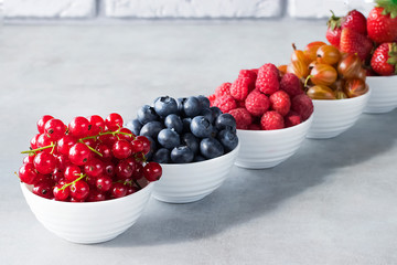 Fresh berries in white bowls on a gray background. Blueberries, strawberry, raspberry, gooseberries and redcurrants.