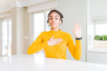 Beautiful african american woman with afro hair wearing a casual yellow sweater Swearing with hand...