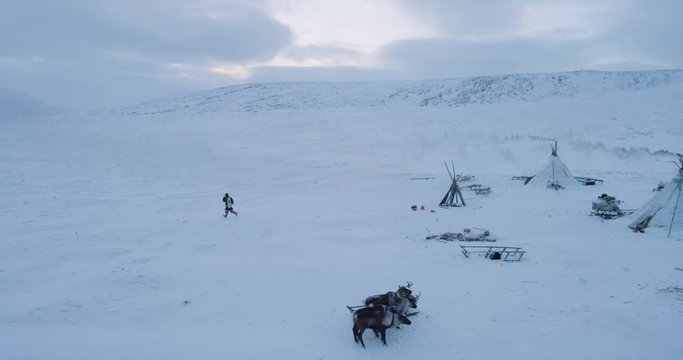 Winter in Arctic aerial view of a big camp of yurts and running man wearing a traditional clothing from fur.