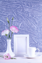 Mockup of picture frame decorated flowers in vase and coffee cup on white table with clean space for text and design your blogging.