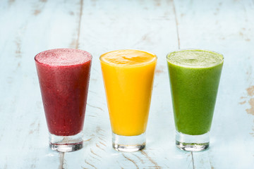 Three colorful fruit smoothies, mango, grape, melon, cabbage, beetroot, lime, on a blue green wood table