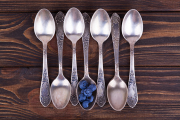 The concept of individuality. Several empty teaspoons and one spoon with berries on a dark wooden...
