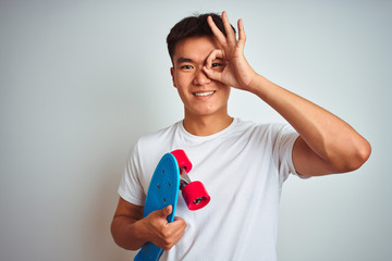 Young asian chinese student man holding skate standing over isolated white background with happy face smiling doing ok sign with hand on eye looking through fingers