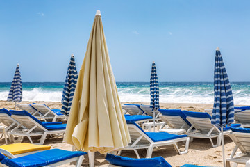 Sun beds with umbrellas on a public sandy beach. Close-up.