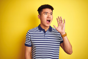 Naklejka premium Young asian chinese man wearing striped polo standing over isolated yellow background shouting and screaming loud to side with hand on mouth. Communication concept.