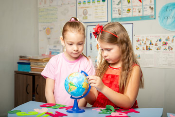 Fototapeta premium Children learn country names in English. girls are holding a globe.
