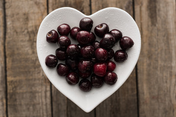top view of red, fresh, whole and ripe cherries covered with droplets on plate on wooden surface