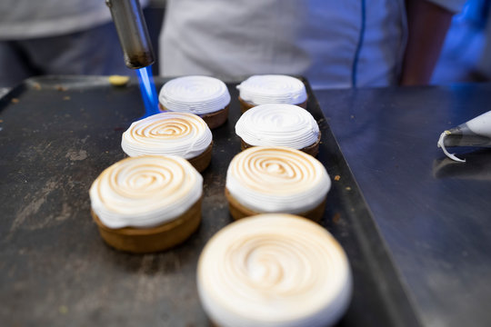From above cooking delicious round cakes topped with whipped cream caramelized by a gas torch on arranged on baking tray