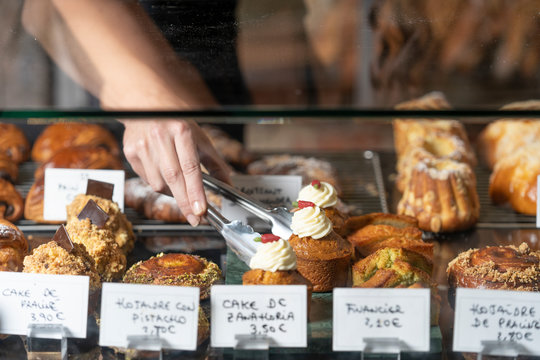 Crop hand of person taking appetizing pastry topped with white cream by metal thongs from cafe counter