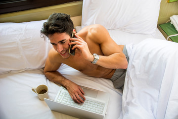 Handsome shirtless muscular young man in bed talking on cell phone placing a call