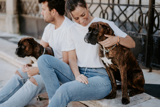 Young people smiling and sitting bonding with cute serious boxer dogs outside