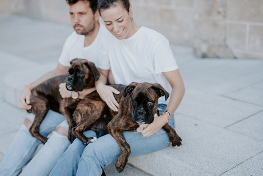 Young people smiling and sitting bonding with cute serious boxer dogs outside