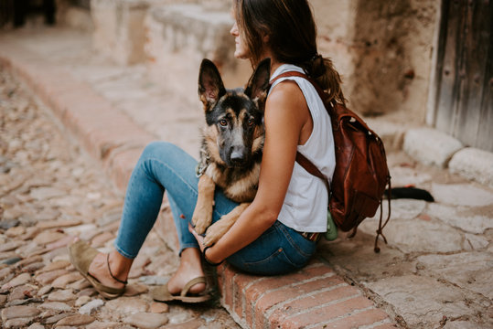 Casual young women sitting on concrete pavement with adorable german shepherd