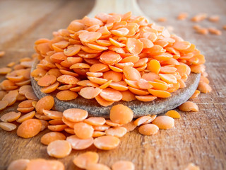 Close up of red lentils split uncooked on wooden spoon and wooden surface