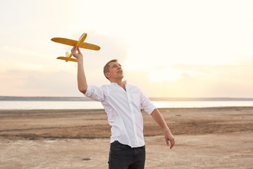 Happy young man playing with toy airplane on the beach on sunset. Dreams of being a child