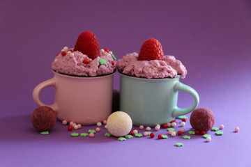 blaue und pink retro kaffeetassen mit einer himbeercreme gefüllt und himbeeren dekoriert außenrum runde Pralinenkugeln und streudekor