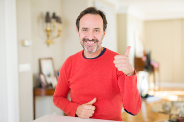 Fototapeta na wymiar Handsome middle age man at home doing happy thumbs up gesture with hand. Approving expression looking at the camera with showing success.