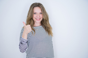 Beautiful blonde girl with blue eyes wearing striped sweater over white isolated background doing happy thumbs up gesture with hand. Approving expression looking at the camera with showing success.