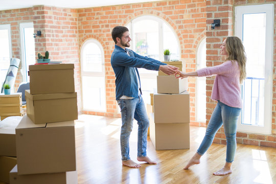 Young couple dancing celebrating moving to new apartment around cardboard boxes