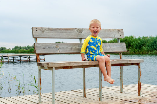 Close-up legs and feet. blond boy is sitting on the bridge. child is inbathing suit by river. Pure authentic emotions