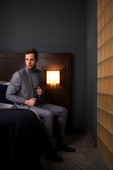 Modisch selbstbewusster Mann im grauen modernen Anzug ist elegant und leger gekleidet sitzt auf einem Bett im Hotel Zimmer