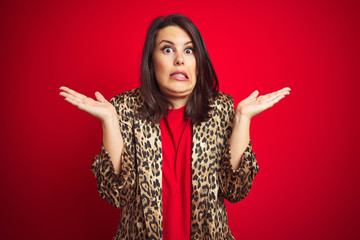 Young beautiful brunette woman wearing a leopard jacket over red isolated background clueless and...