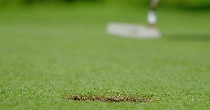A successful rack focus shot of a golf ball with an alignment line drawn onto the ball to improve accuracy drops into the cup