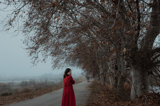 Dreamy woman in red dress walking along empty road of hazed mysterious terrain