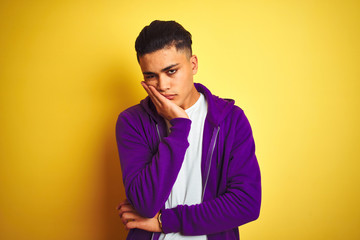 Young brazilian man wearing purple sweatshirt standing over isolated yellow background thinking looking tired and bored with depression problems with crossed arms.