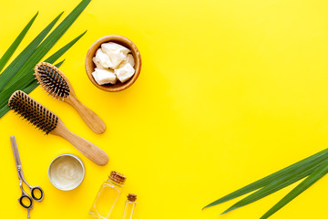 Fototapeta na wymiar Cosmetics for hair care with jojoba, argan or coconut oil in bottle, comb, scissors on yellow background top view mockup