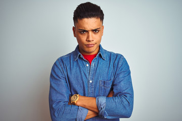 Young brazilian man wearing denim shirt standing over isolated white background skeptic and nervous, disapproving expression on face with crossed arms. Negative person.