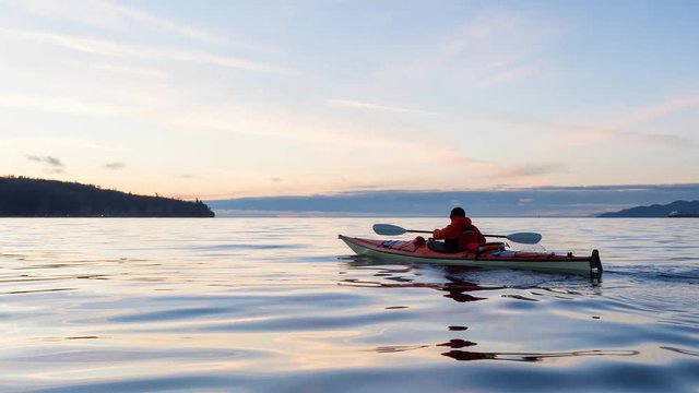 Adventure Man on a Sea Kayak is kayaking during a vibrant and colorful winter sunset. Taken in Vancouver, British Columbia, Canada. Still Image Continuous Animation
