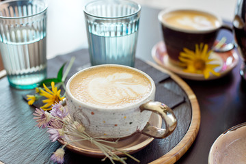 Different types of coffee in a cup on a dark table, two glasses with cold water and spring flowers on the table, top view